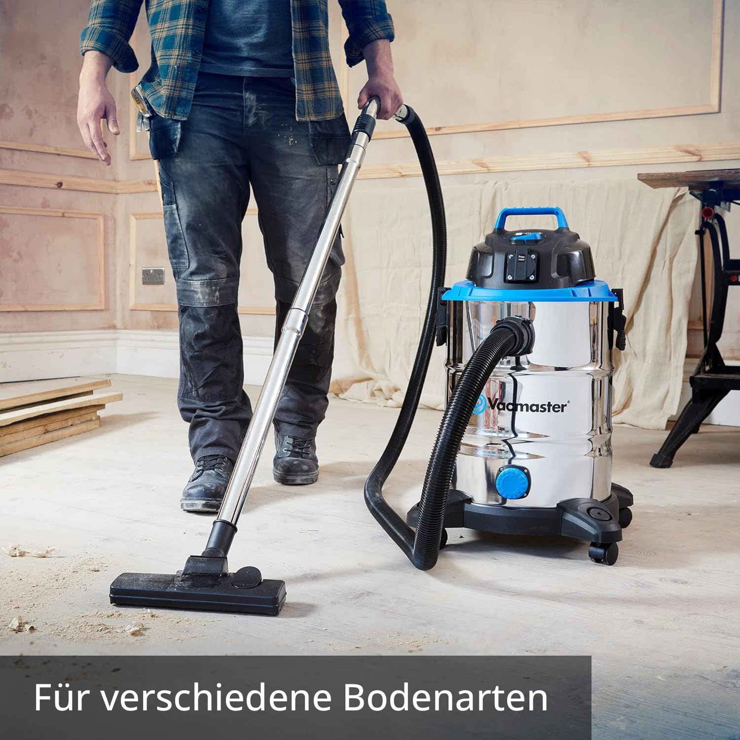 Ein Mann saugt einen staubigen Boden mit einem silbernen Nass-/Trockensauger.