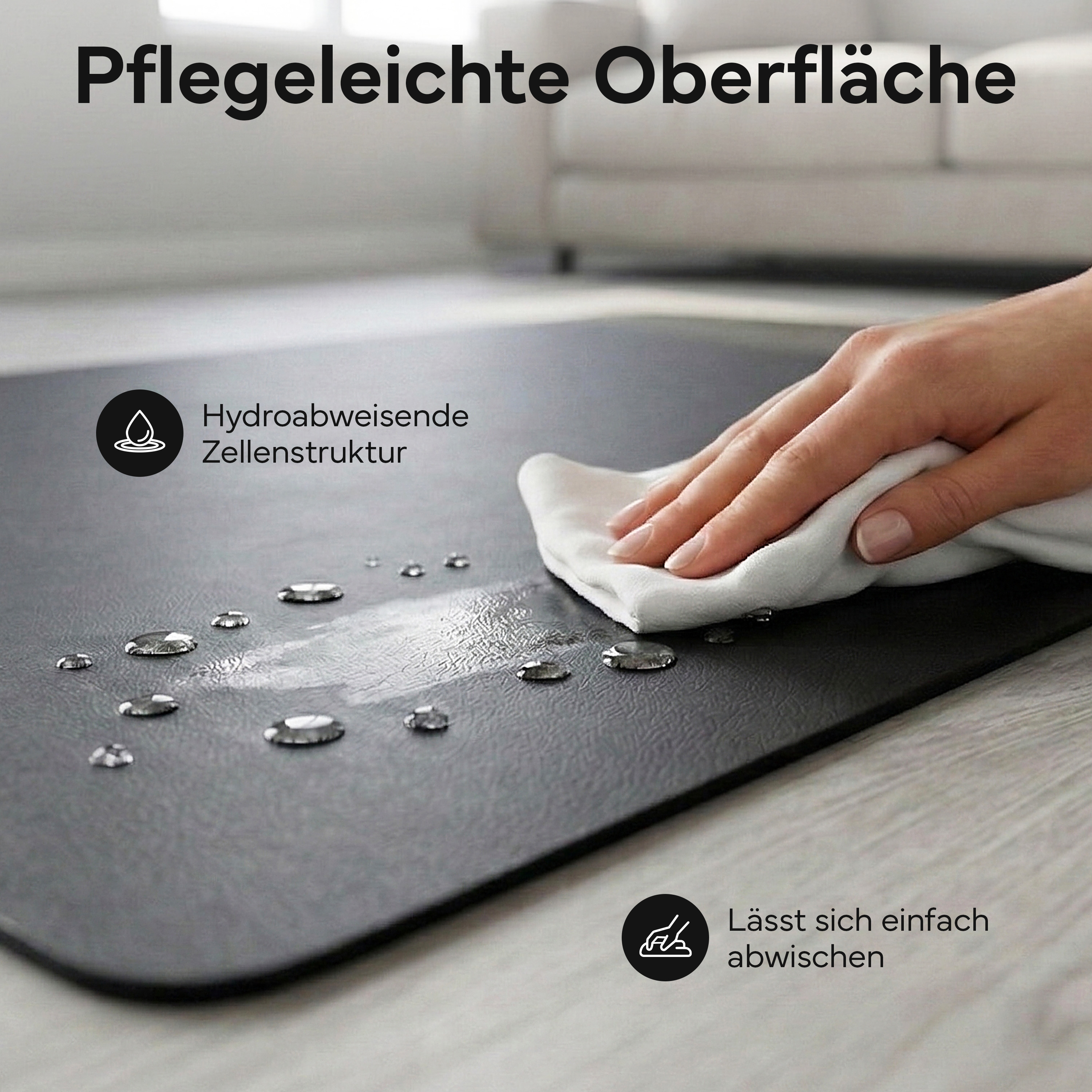 Eine Hand wischt Wasser von einer dunklen, wasserabweisenden Matte.