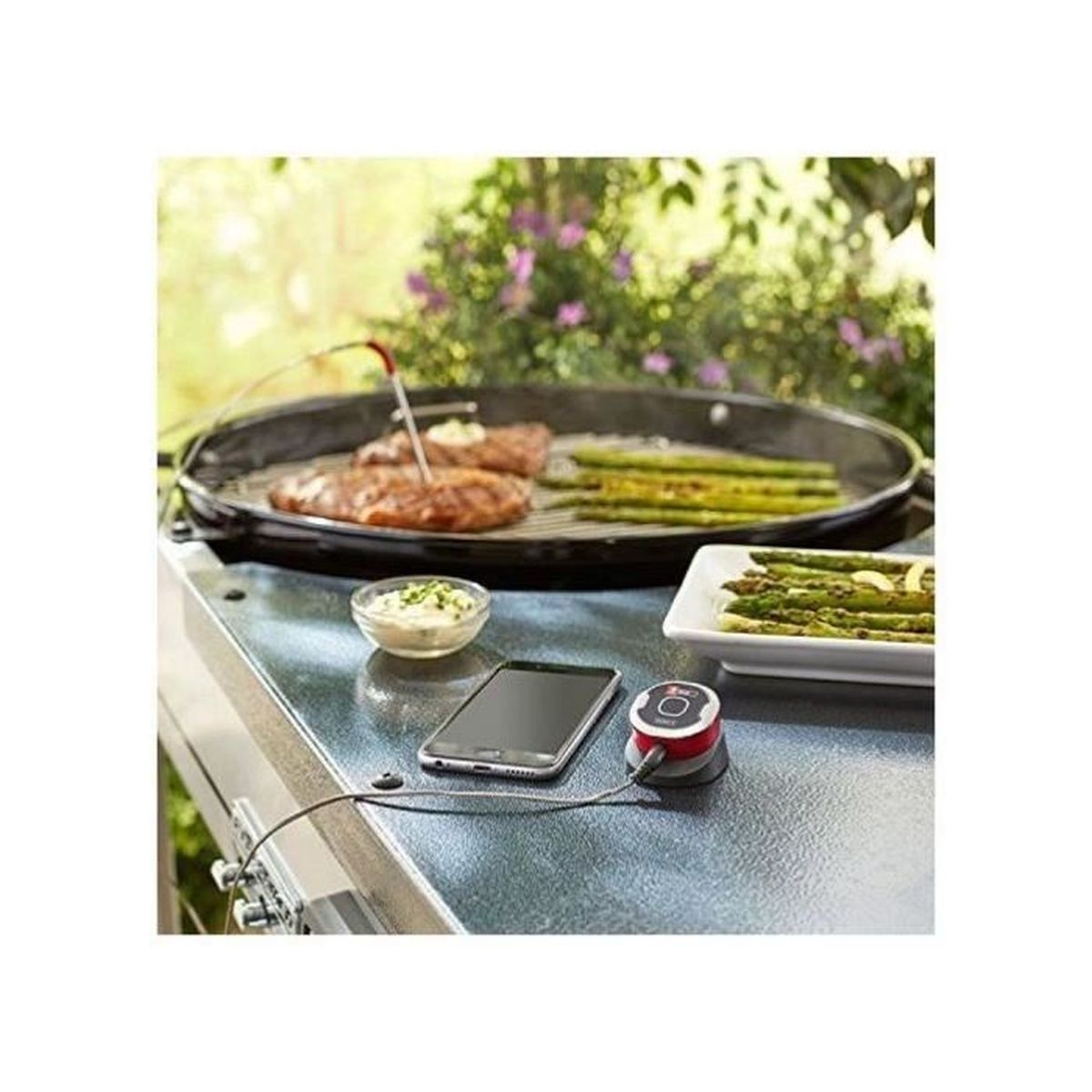 Fleisch und Spargel werden auf einem Grill zubereitet, daneben liegen ein Handy und ein Thermometer.