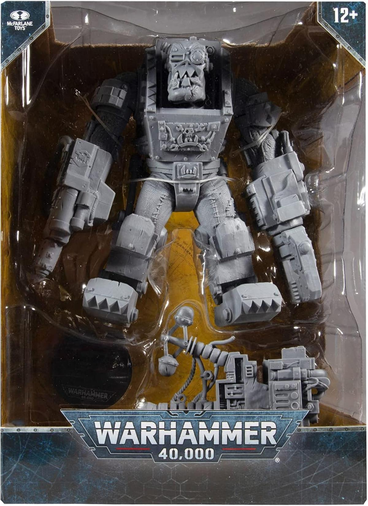 Graue Warhammer 40.000 Ork-Figur in der Verpackung mit Waffen und Zubehör.