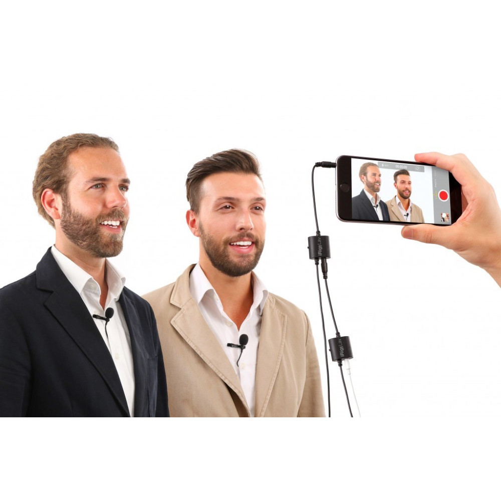 Dwóch mężczyzn z mikrofonami przypinanymi do klapy jest filmowanych przez smartfon.