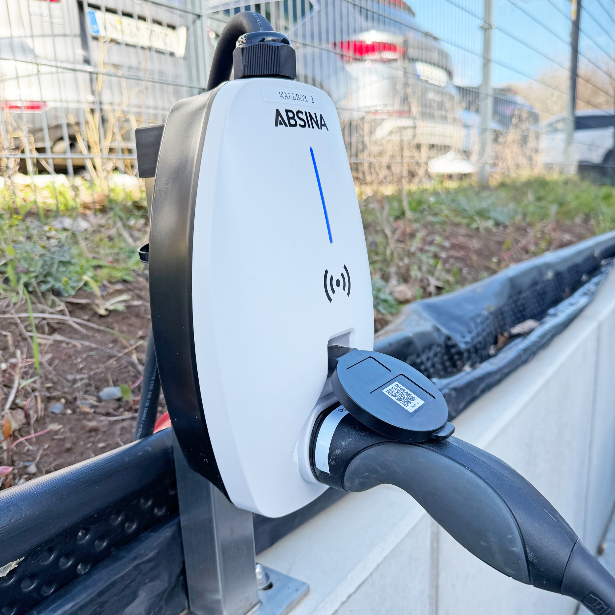 Eine weiße ABSINA Wallbox 2 Ladesäule mit angeschlossenem schwarzen Kabel und Stecker.