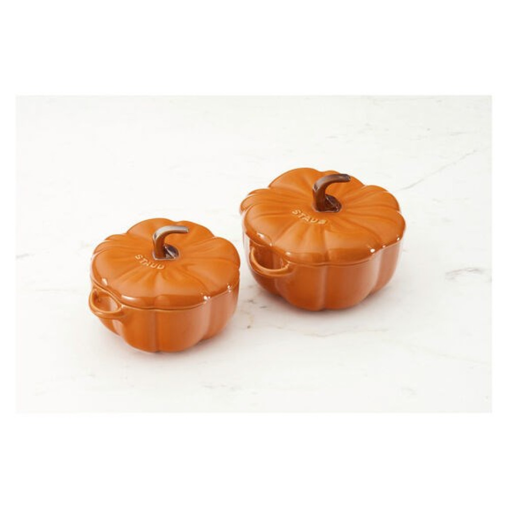 Dwa pomarańczowe garnki w kształcie dyni z uchwytami i pokrywkami siedzą obok siebie.