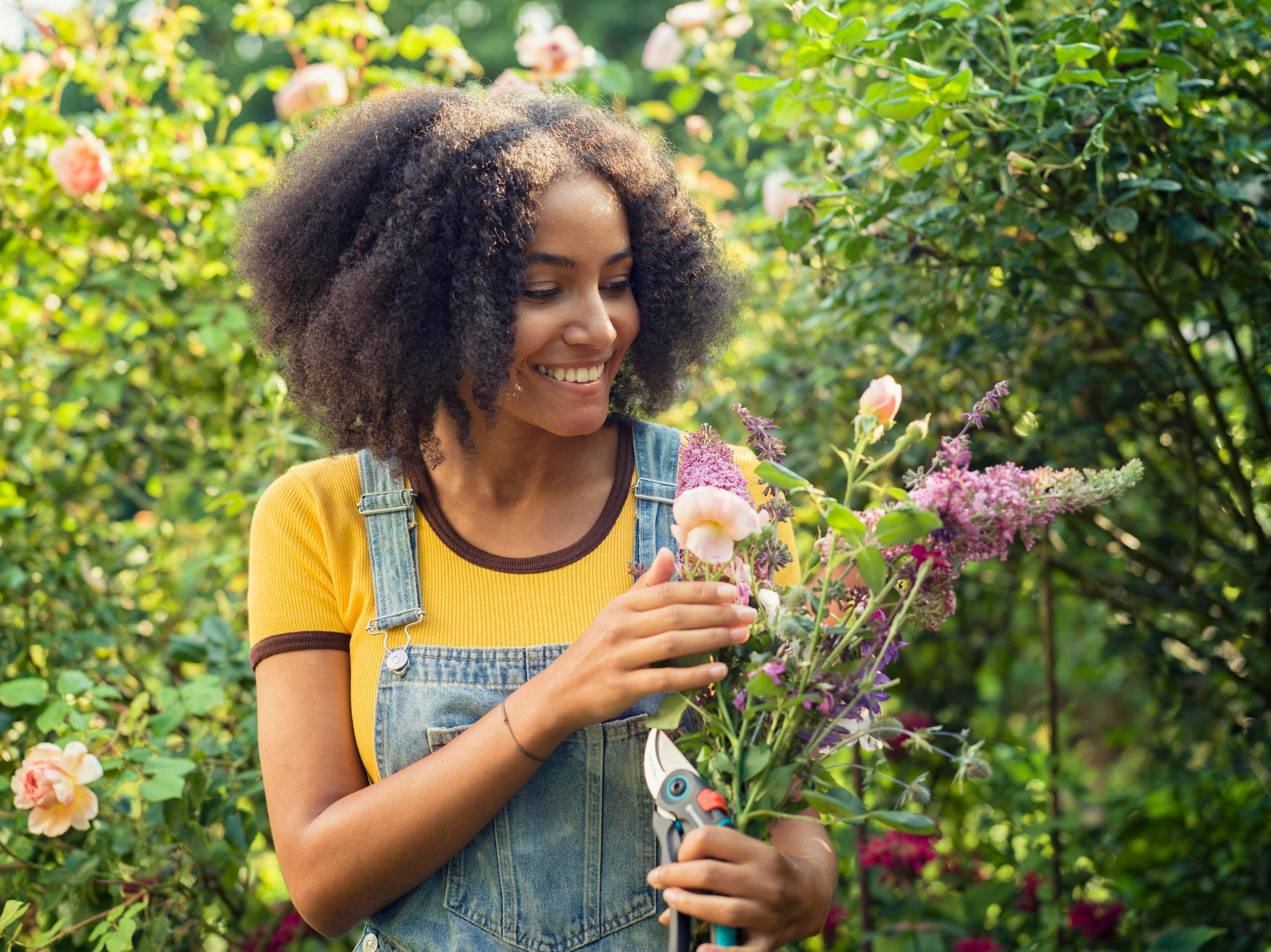Eine Frau mit lockigem Haar hält Blumen und eine Gartenschere.