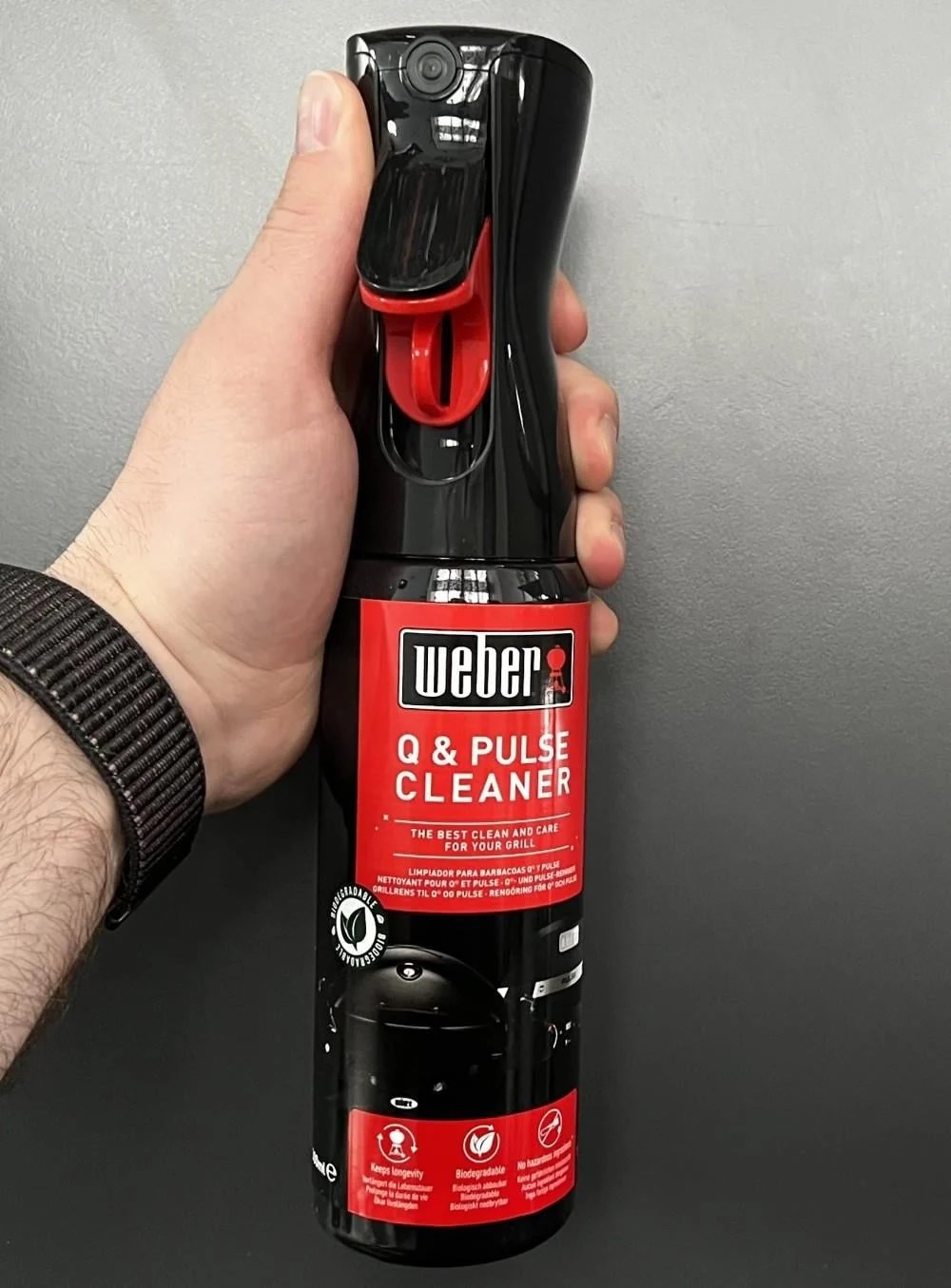 Hand hält eine schwarze Weber Q & Pulse Reiniger Sprühflasche mit rotem Sprühkopf.