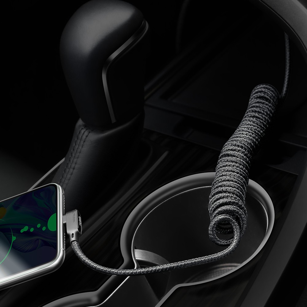 Ein gewickeltes dunkelgraues Ladekabel verbindet ein Smartphone mit der Mittelkonsole eines Autos.