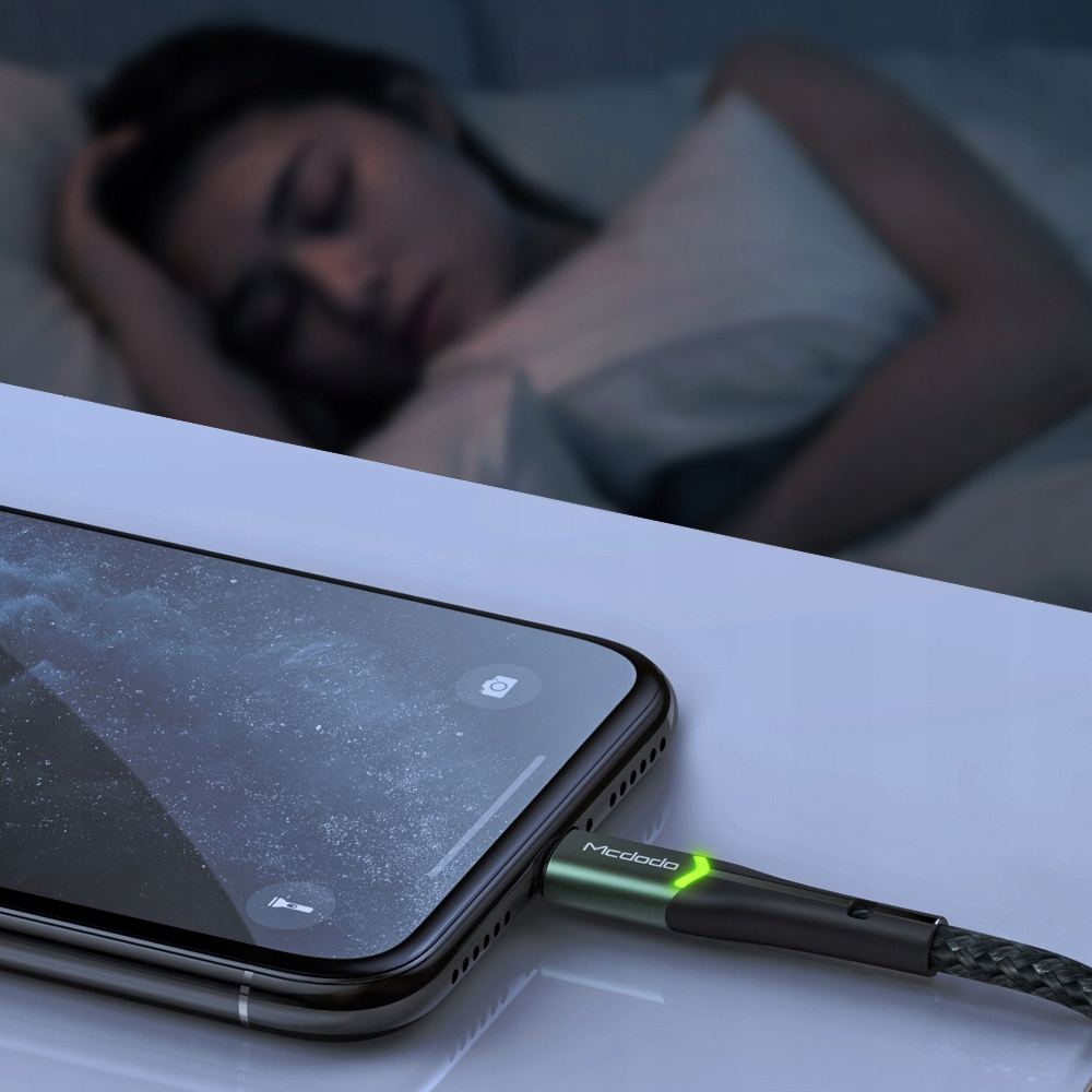 Ein Handy wird aufgeladen, während eine Person schläft. Das Ladekabel hat eine grüne LED.
