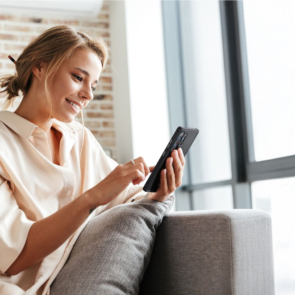 Eine Frau sitzt auf einem Sofa und benutzt ihr Handy. Sie trägt ein helles Hemd.