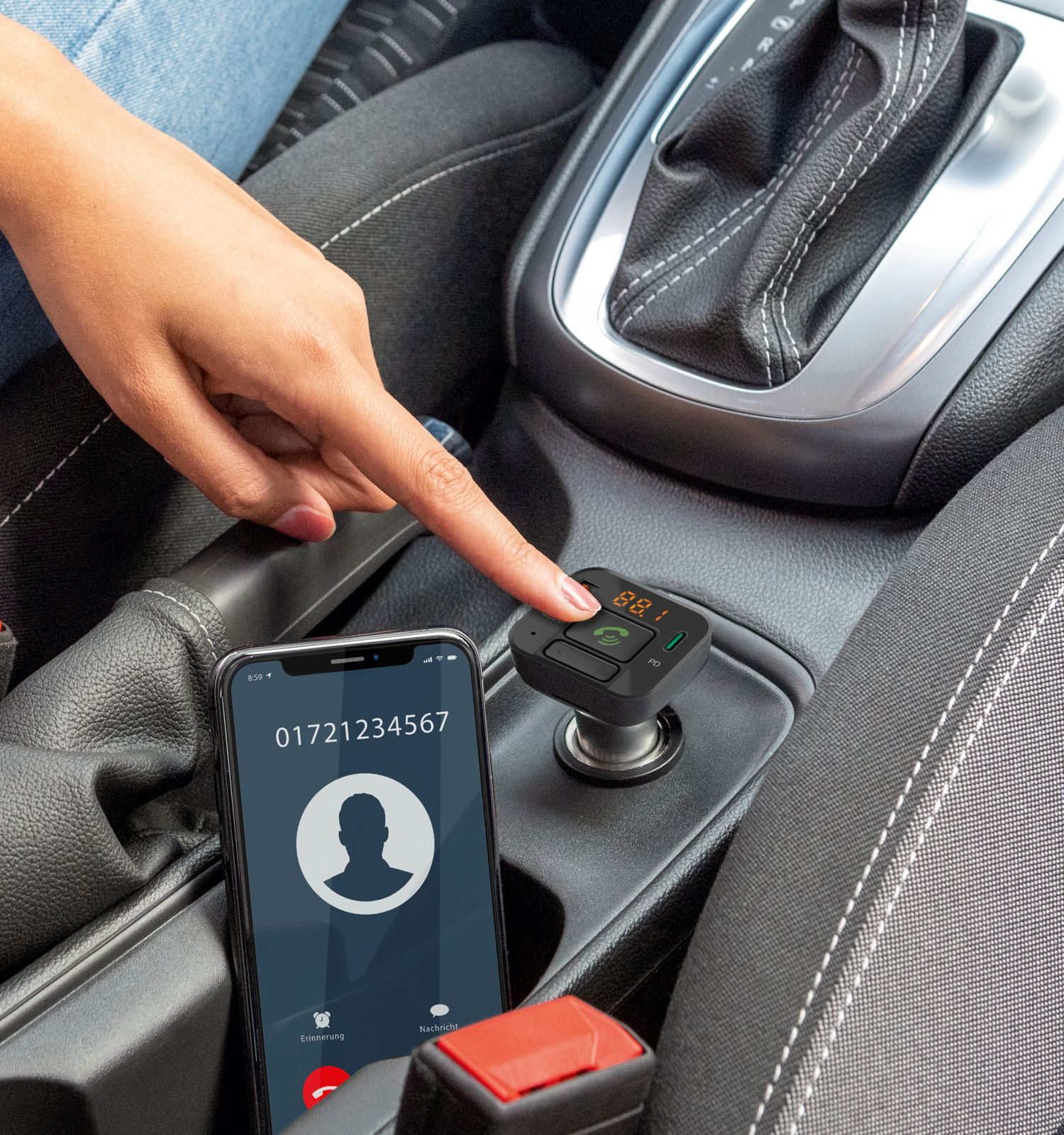 Una mano preme un pulsante su un caricatore per auto nero, con uno smartphone accanto.
