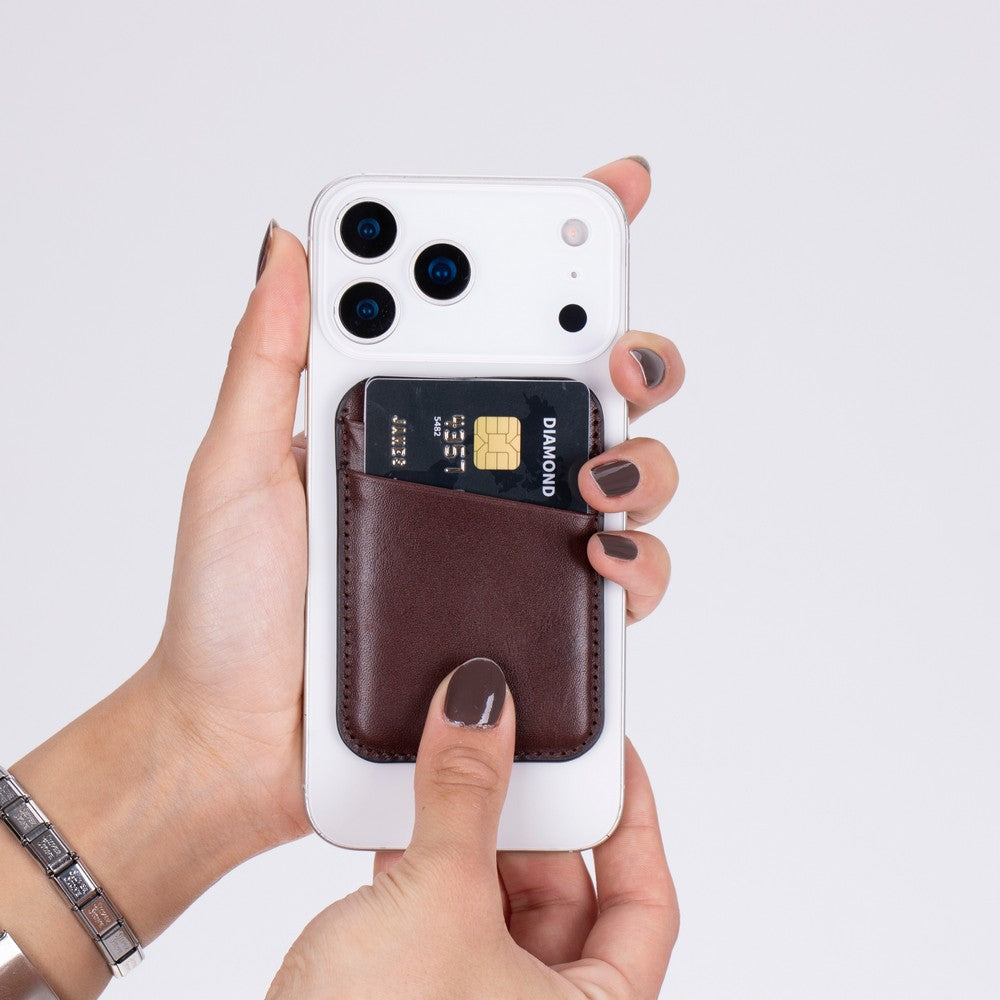Kahverengi telefon cüzdanı, beyaz iPhone üzerinde kredi kartı, eller tarafından tutuluyor.