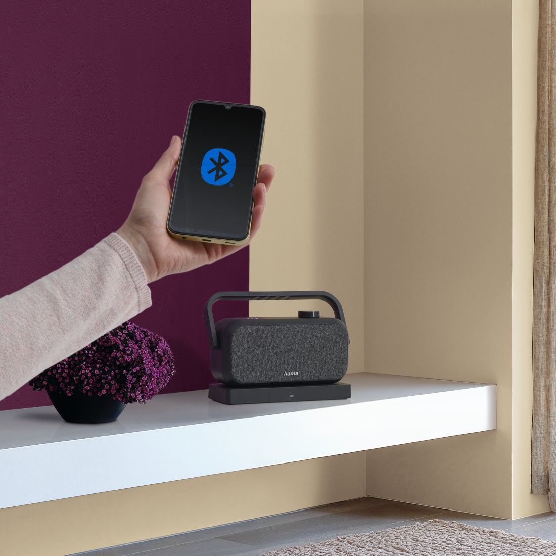 Ręka trzyma smartfon z symbolem Bluetooth przed głośnikiem.