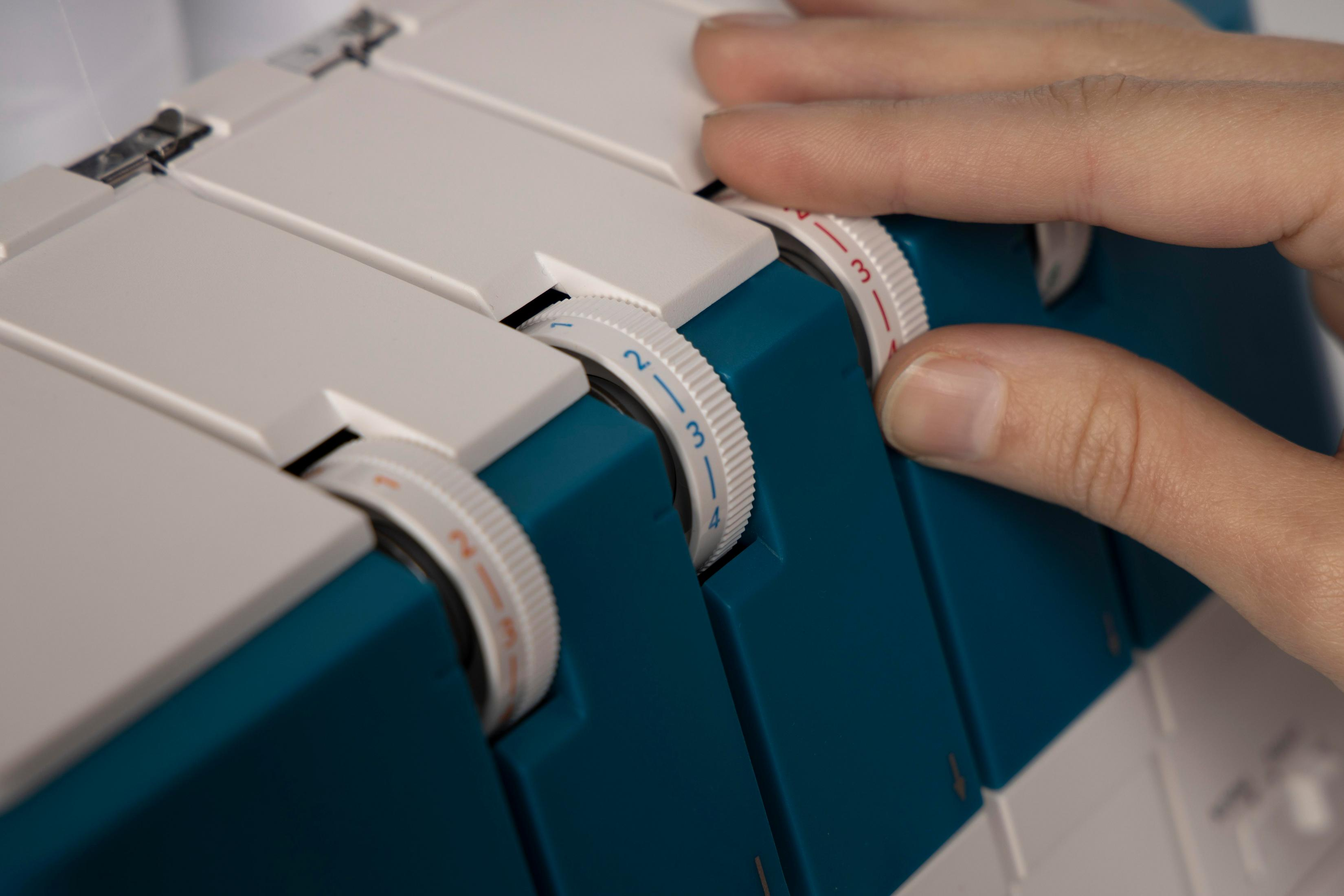Una mano gira un dial en una máquina de coser con partes azules y blancas.