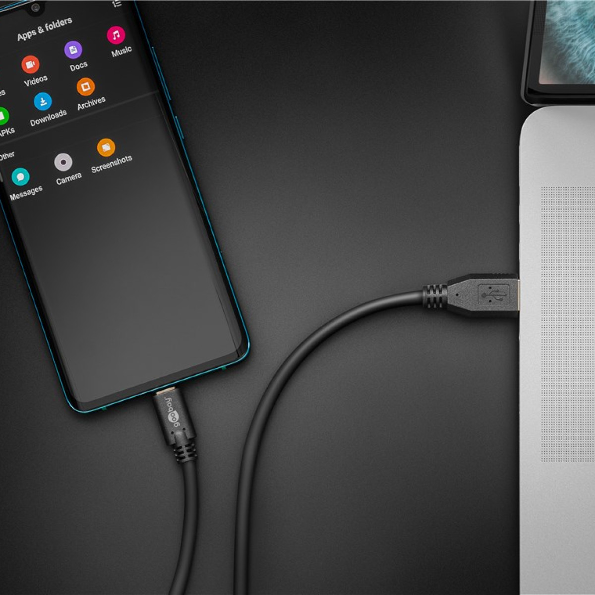 Ein Handy mit Apps ist über USB mit einem Laptop auf dunkler Fläche verbunden.