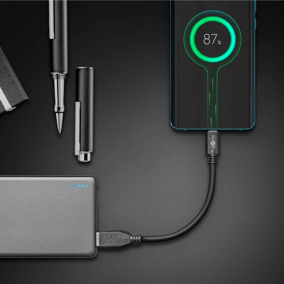 Ein Smartphone wird von einer Powerbank aufgeladen. Daneben liegen Stifte.