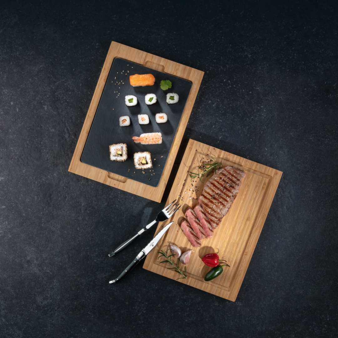 Gegrilltes Steak und Sushi auf Bambustafeln mit Besteck, Knoblauch und Pfeffer.