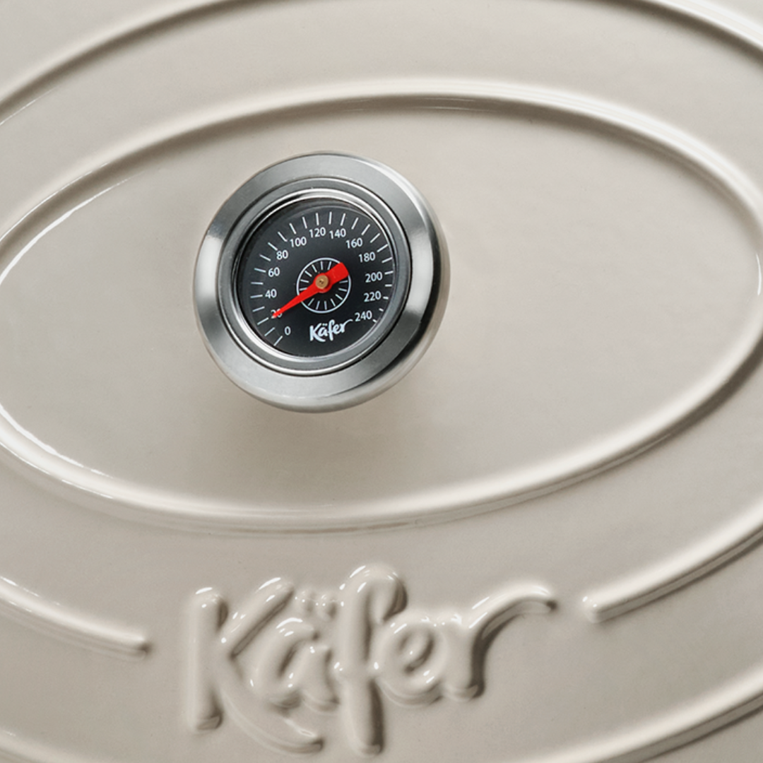 Ein Thermometer auf einem cremefarbenen Topfdeckel mit eingeprägtem Schriftzug.