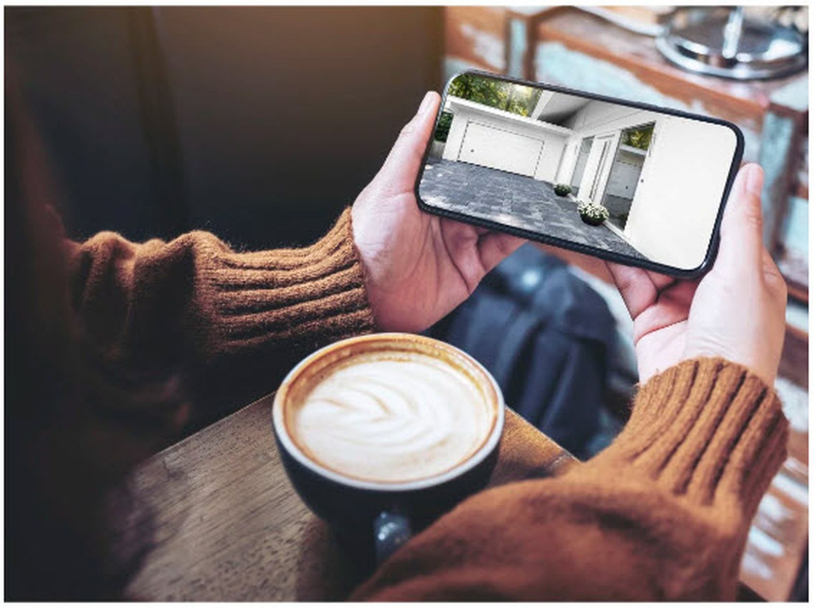 Osoba trzyma smartfon z widokiem garażu obok filiżanki kawy.