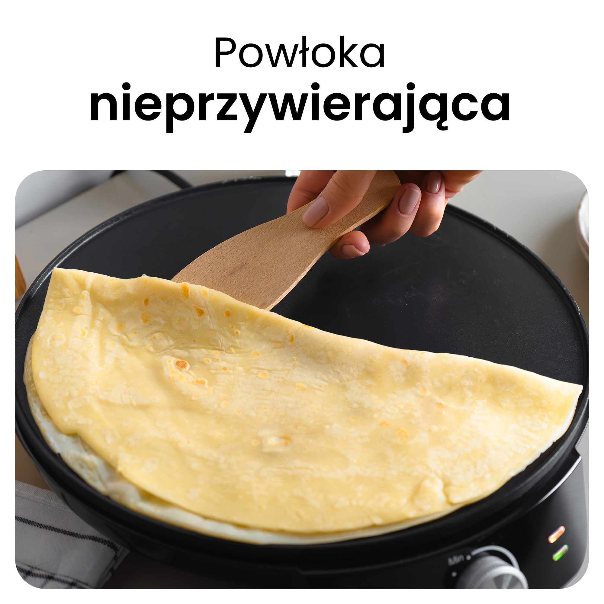 Ręka używa drewnianej łopatki do przewracania naleśnika na czarnej patelni.