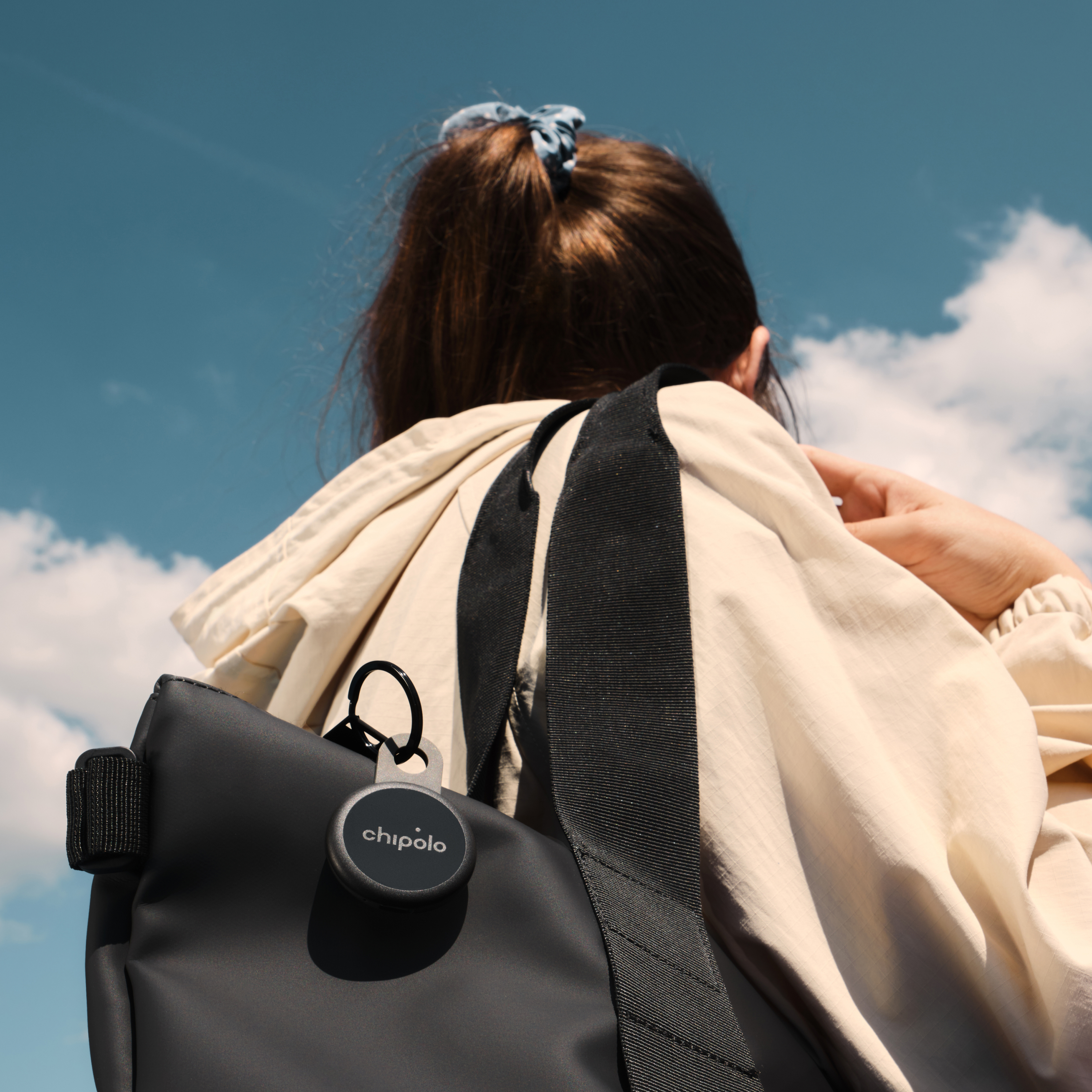 Eine Person mit einem Chipolo-Tracker an einer schwarzen Tasche vor blauem Himmel.