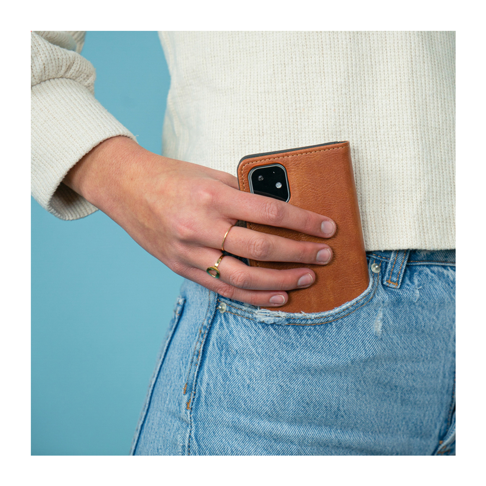 Een persoon stopt een bruine telefoonhoes in een jeanszak.