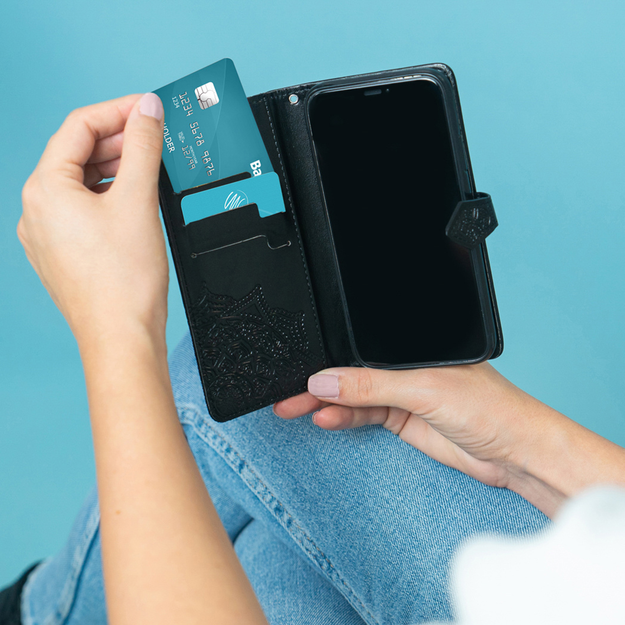 Una mano inserisce una carta di credito blu in un portafoglio nero con un telefono.