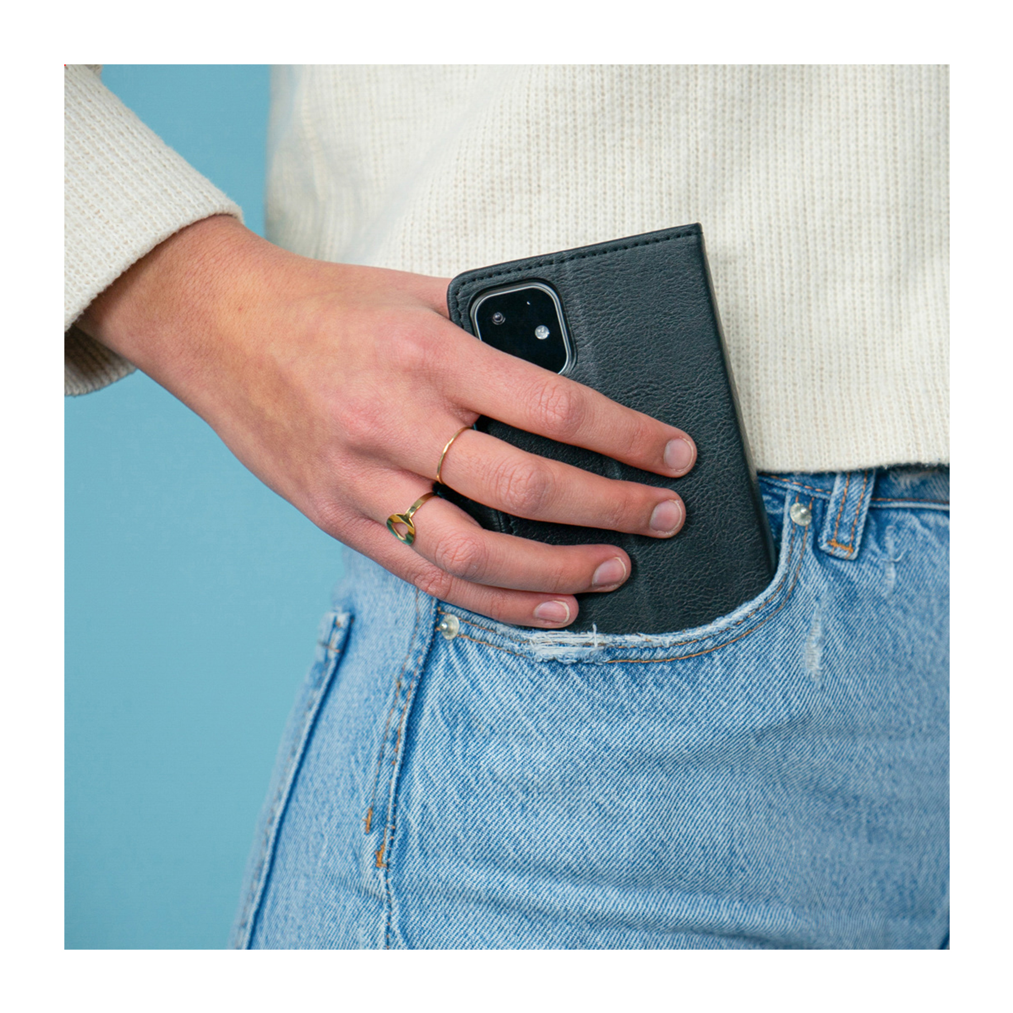 Une main avec des bagues glisse un téléphone noir dans une poche en jean.