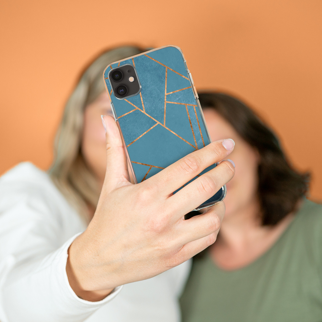 Une main tient un téléphone à motif marbre bleu et lignes dorées devant deux personnes floues.