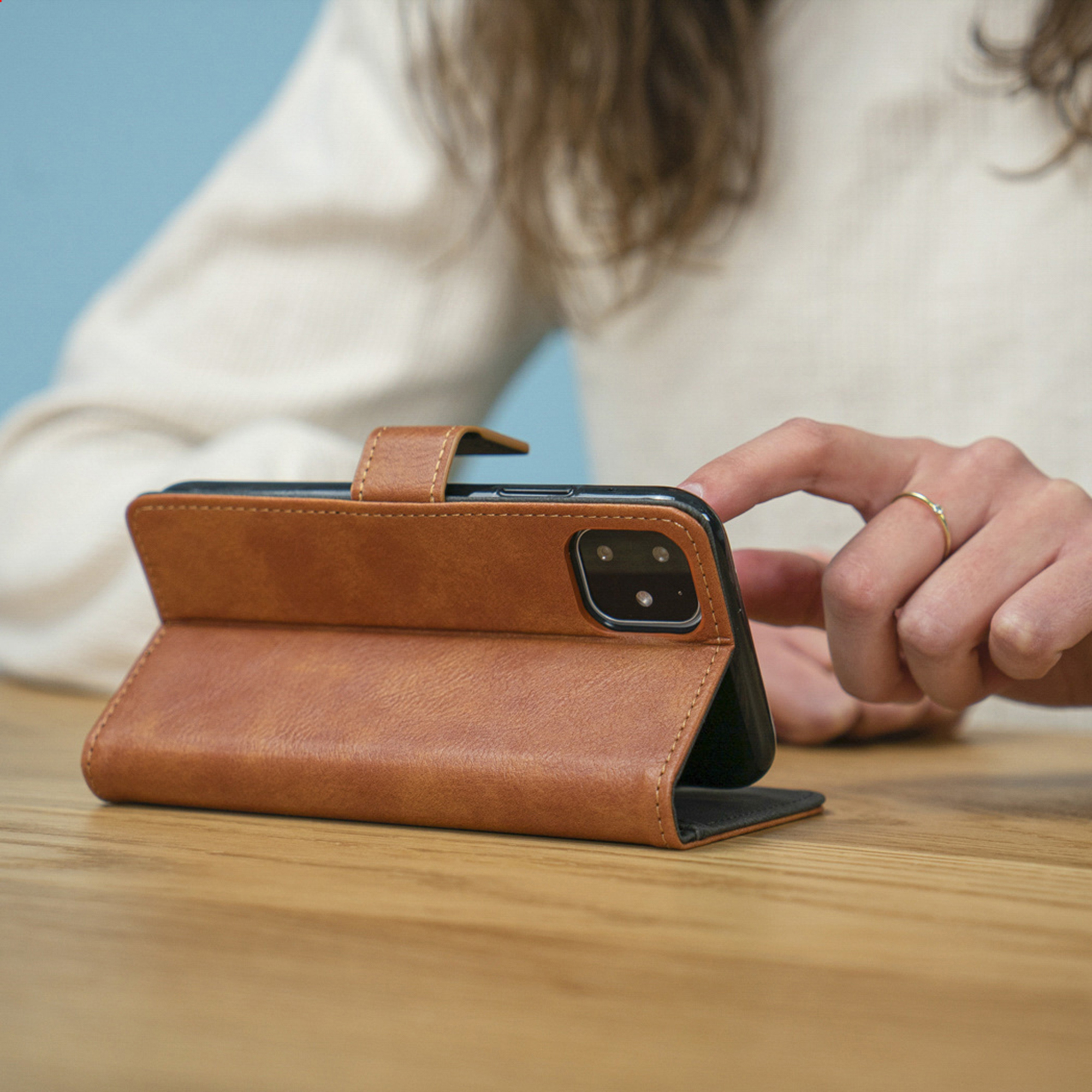 Persoon met bruin telefoonhoesje op houten tafel.