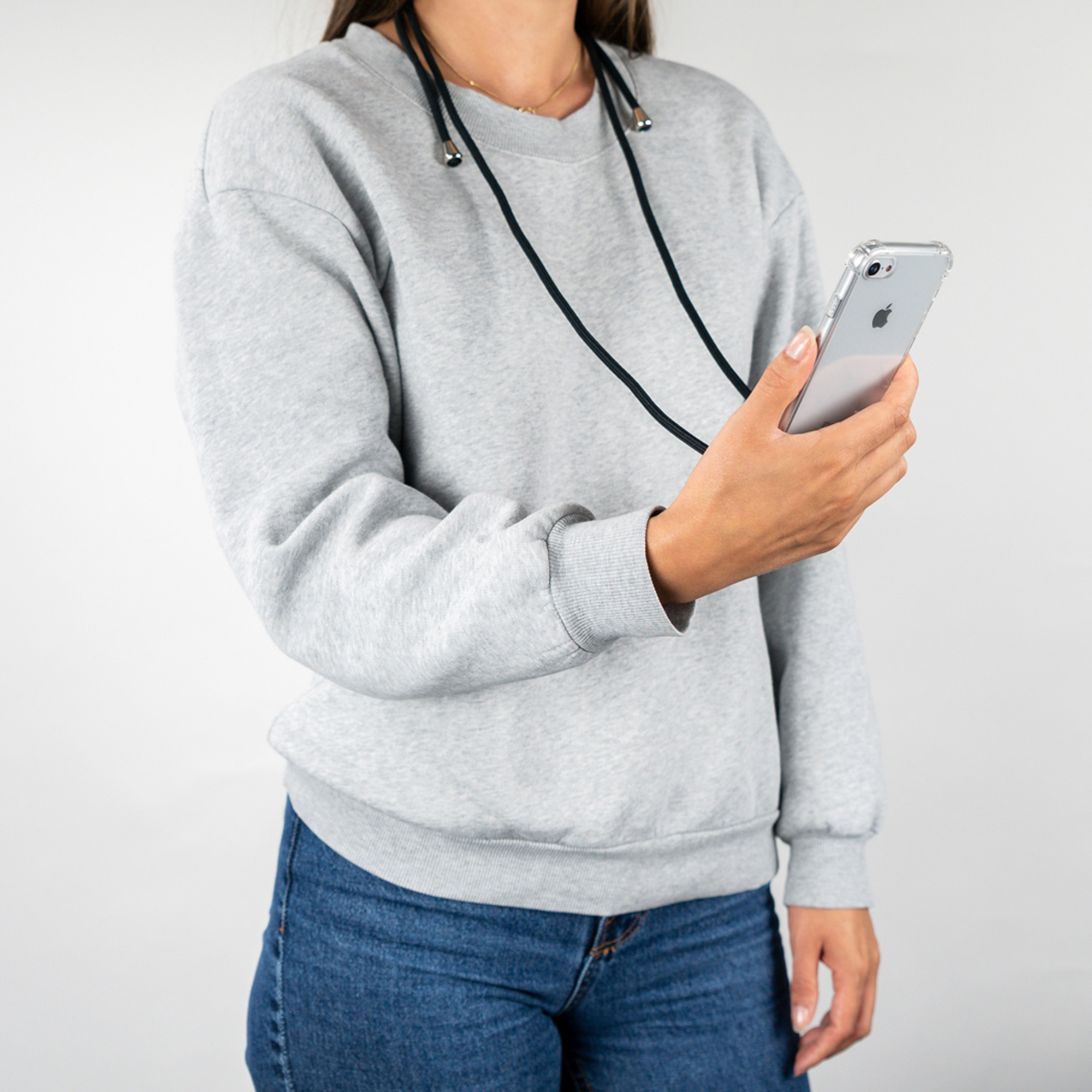 Donna con felpa grigia e jeans che tiene uno smartphone con cordino.