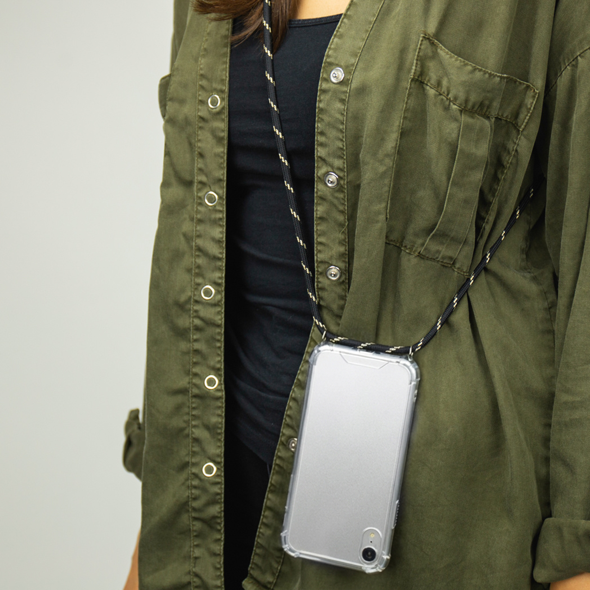 Une personne porte une veste vert olive sur un t-shirt noir avec une lanière de téléphone.