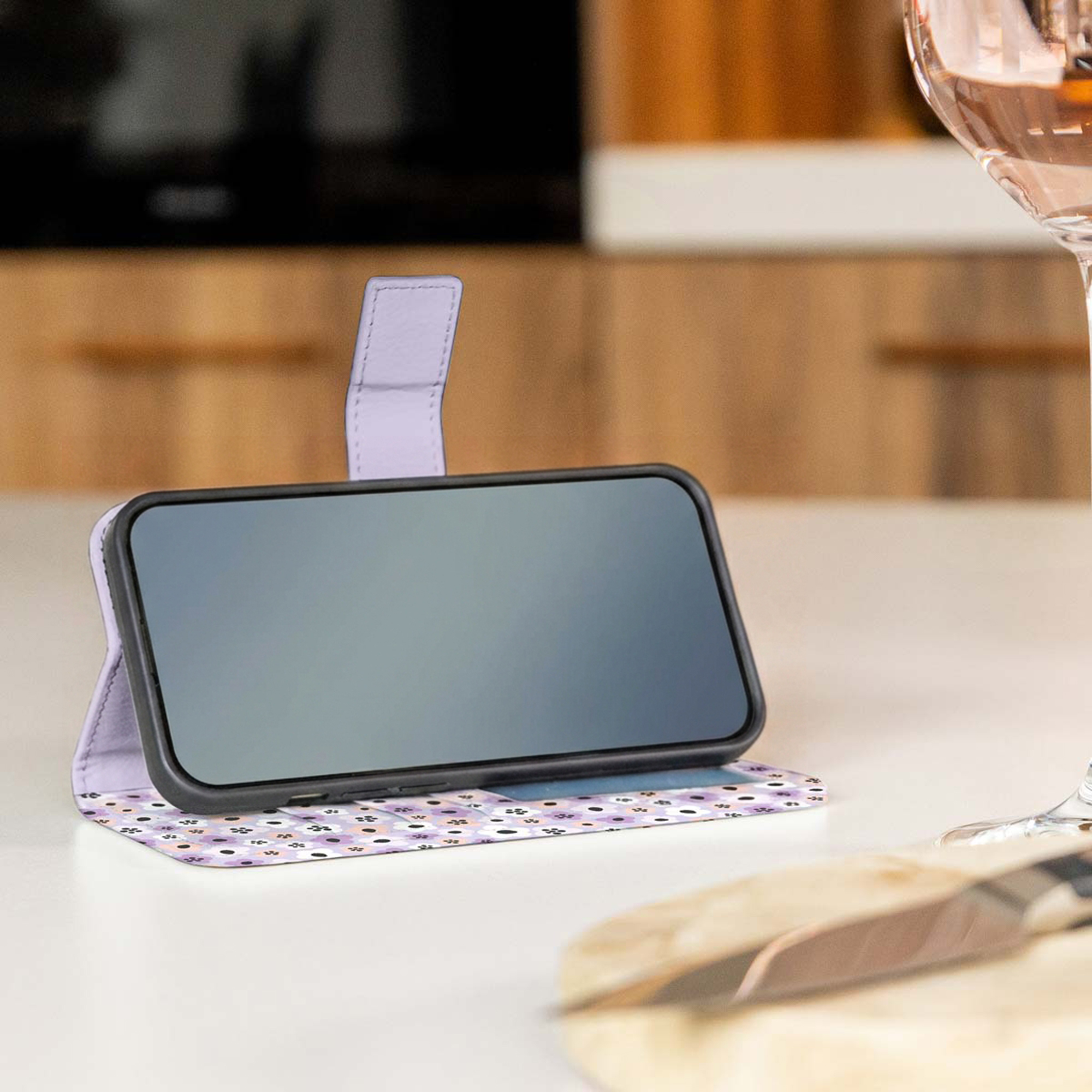 Een telefoon in een paarse bloemenhoes staat op een tafel.