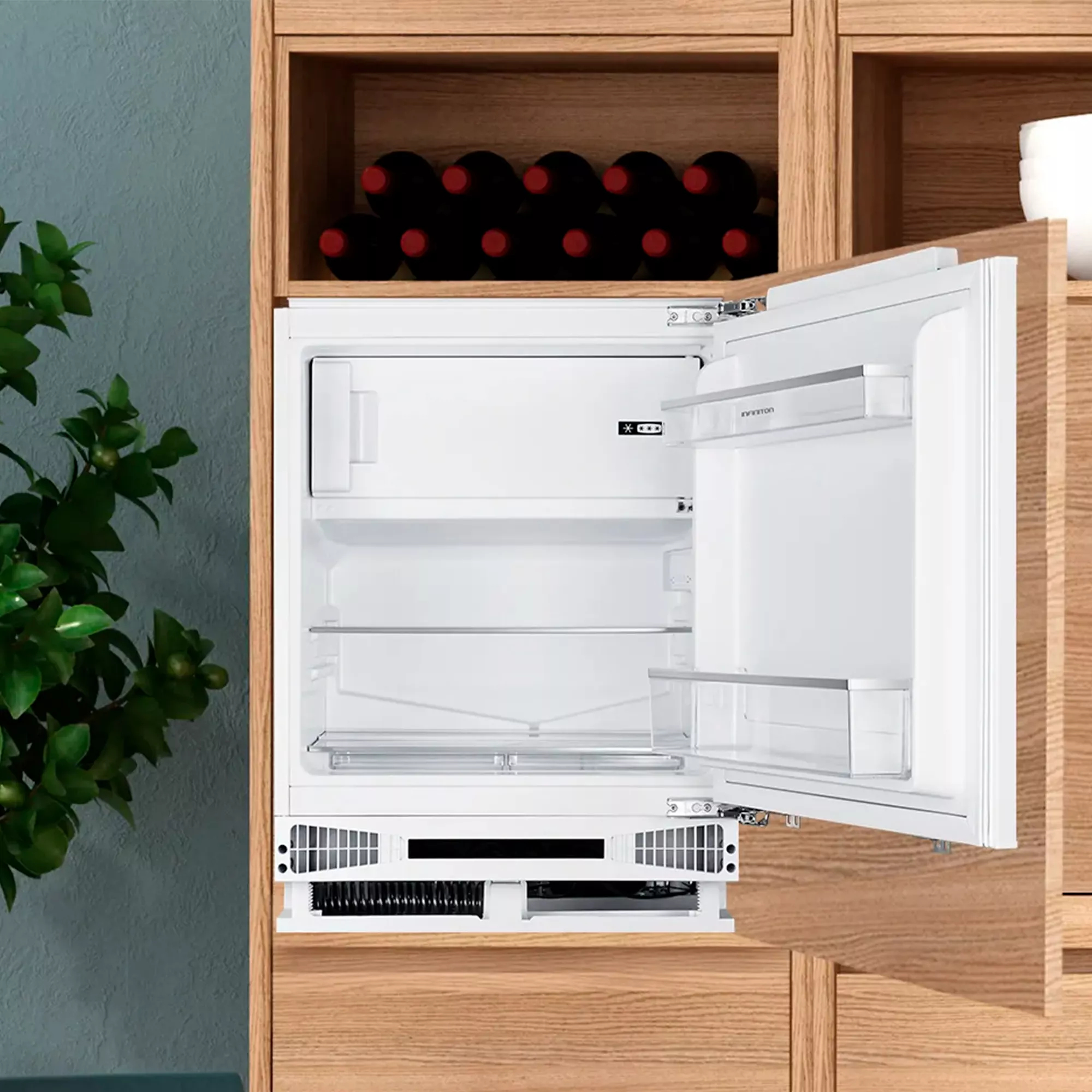 Un refrigerador blanco abierto con estantes de vidrio, junto a gabinetes de madera con botellas de vino.