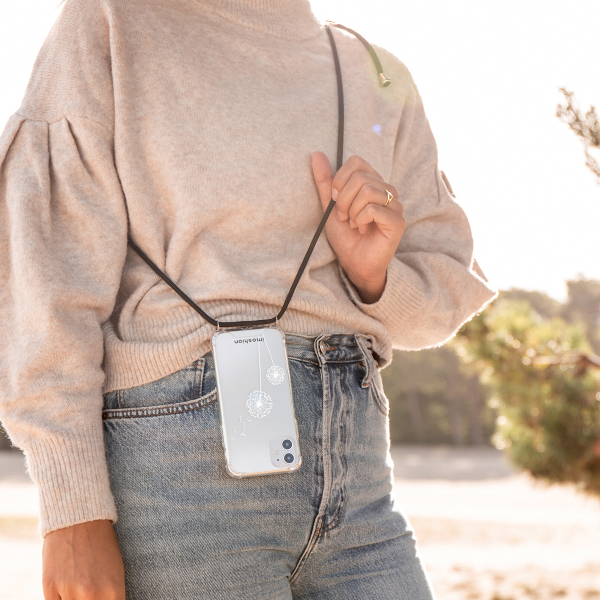 Een persoon met trui en jeans, met een telefoon hangend aan een koord.