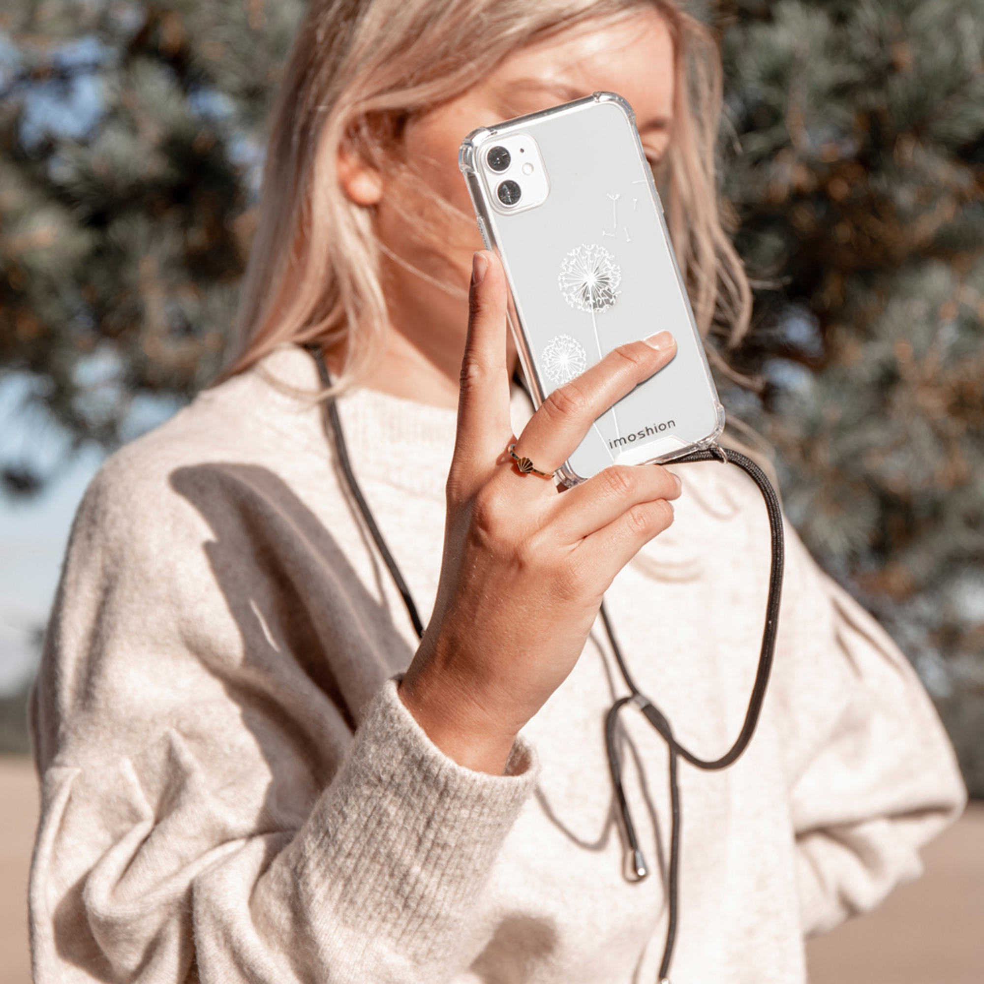 Een vrouw houdt een doorzichtige telefoon met bloemenprint vast. Ze draagt een trui.