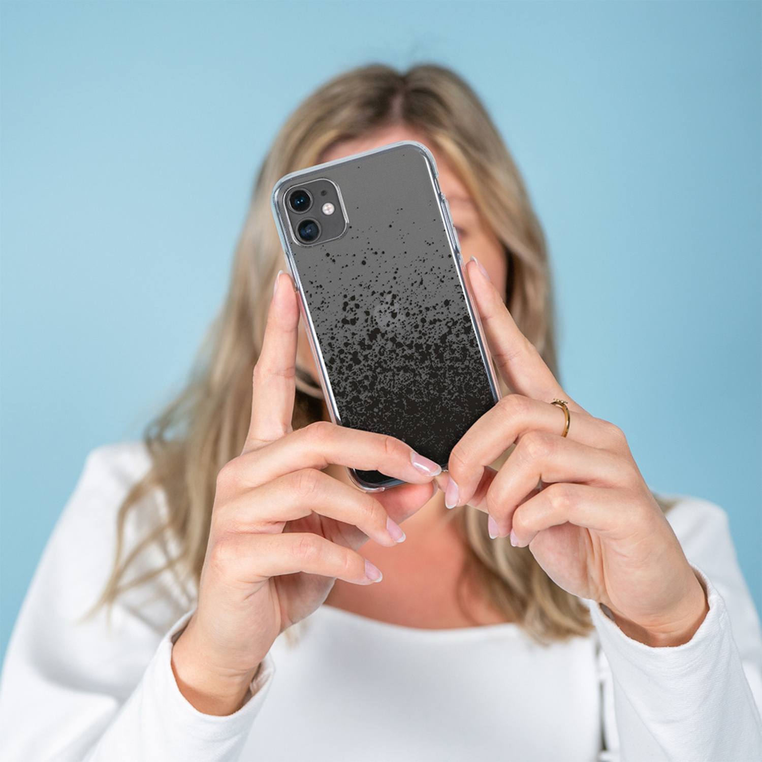 Une femme tient un smartphone à motif éclaboussures noires devant son visage.