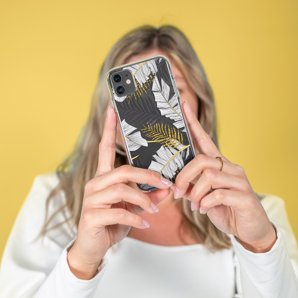 Vrouw houdt telefoon met bladerpatroon vast. Gele achtergrond.