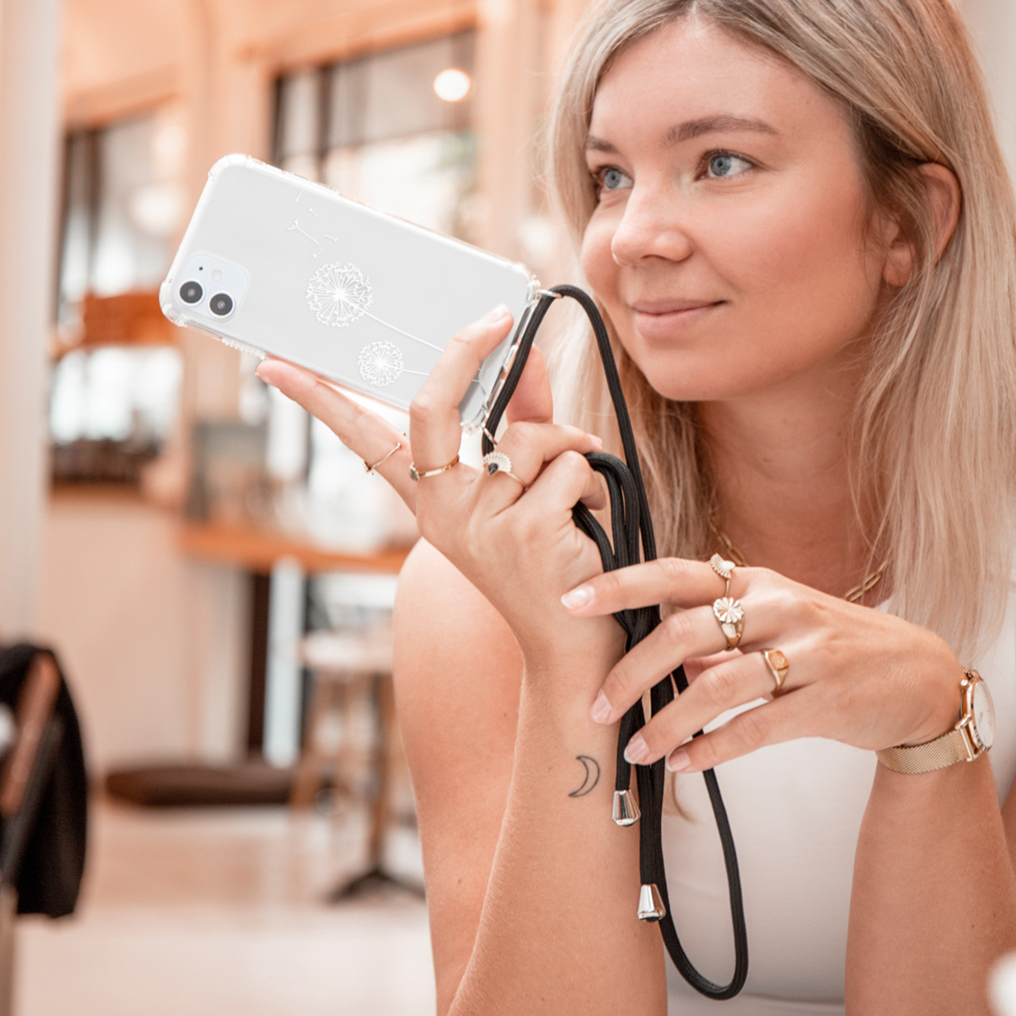Een vrouw houdt een smartphone vast met een paardenbloemmotief en een zwart koord.