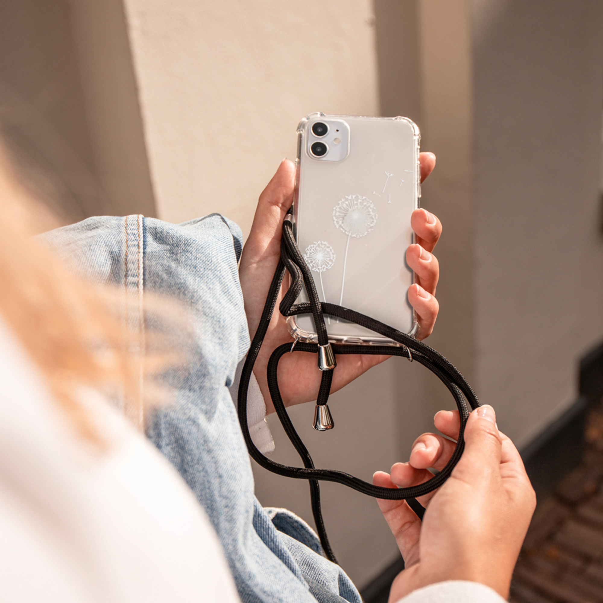 Een persoon houdt een smartphone met een doorzichtige hoes en draagband vast.