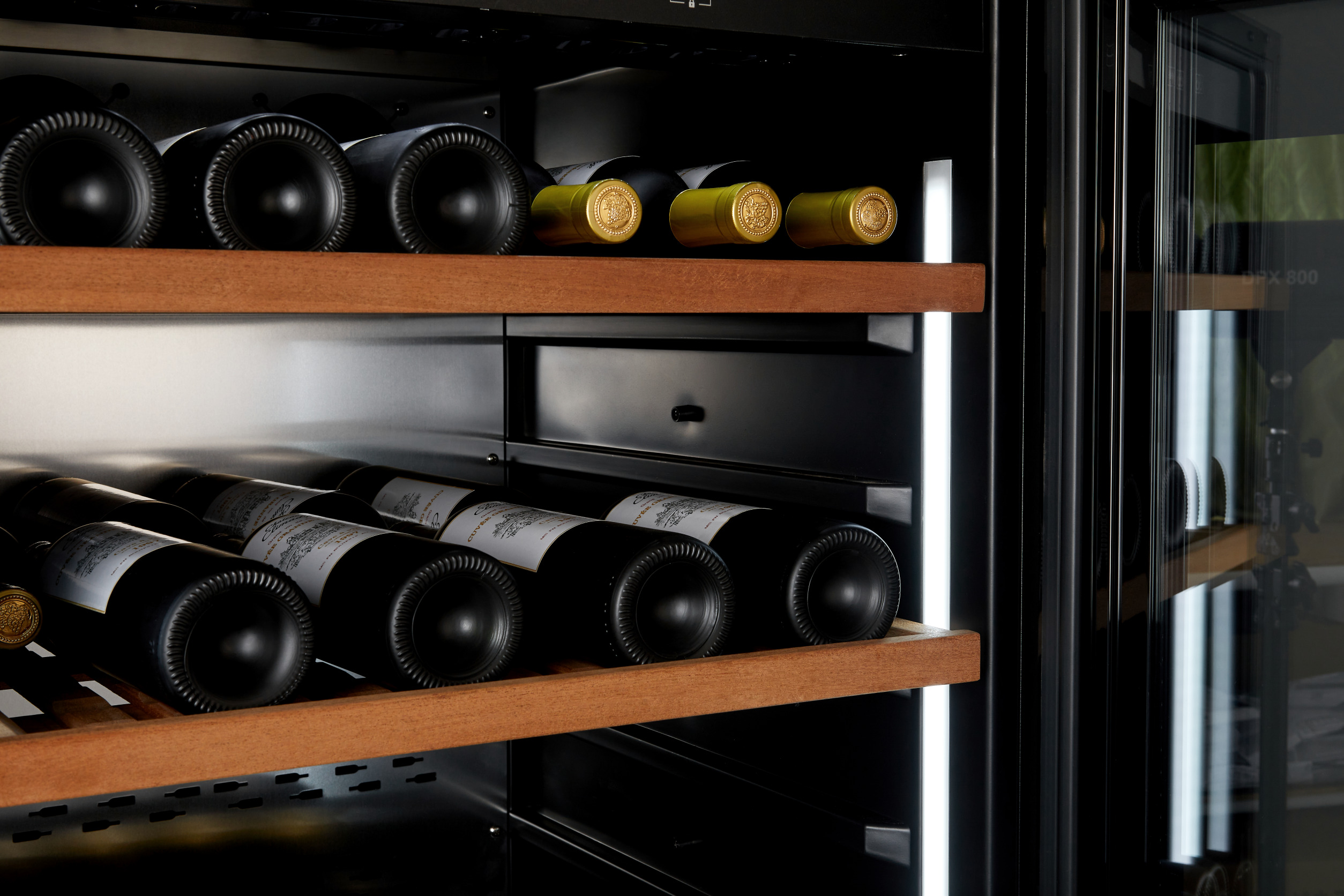 Nevera de vino con estantes de madera, con botellas de vino negras y amarillas.