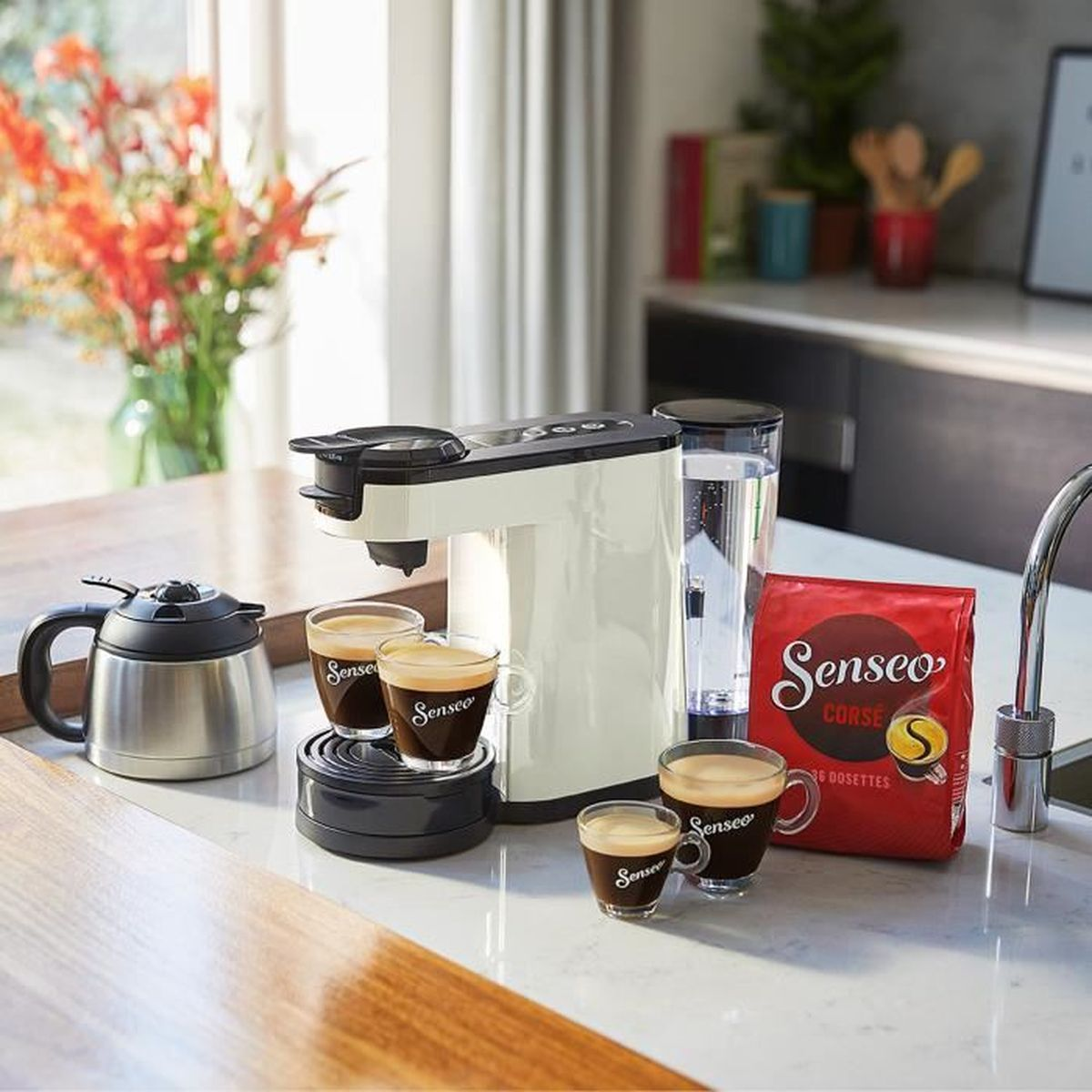 Una macchina da caffè bianca con tre tazze di caffè, una caffettiera termica e una confezione di caffè Senseo.