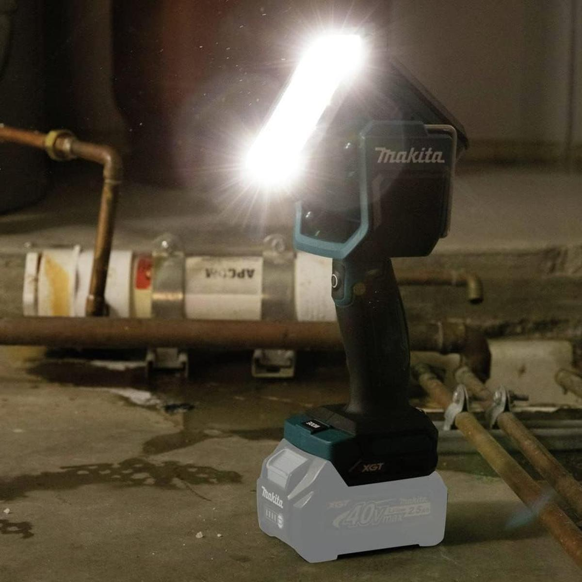 Un faretto Makita luminoso con batteria illumina tubi e pavimento in cemento.
