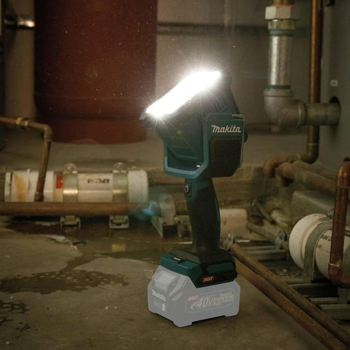 Una lampada da lavoro Makita con batteria si trova su un pavimento di cemento bagnato vicino a tubi.
