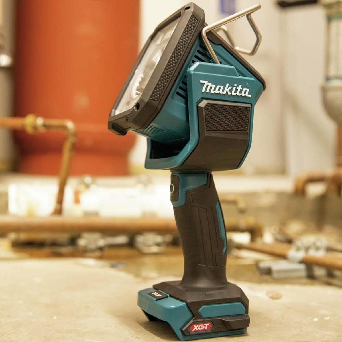 Una lampada da lavoro a batteria Makita turchese con manico in metallo su pavimento in cemento.