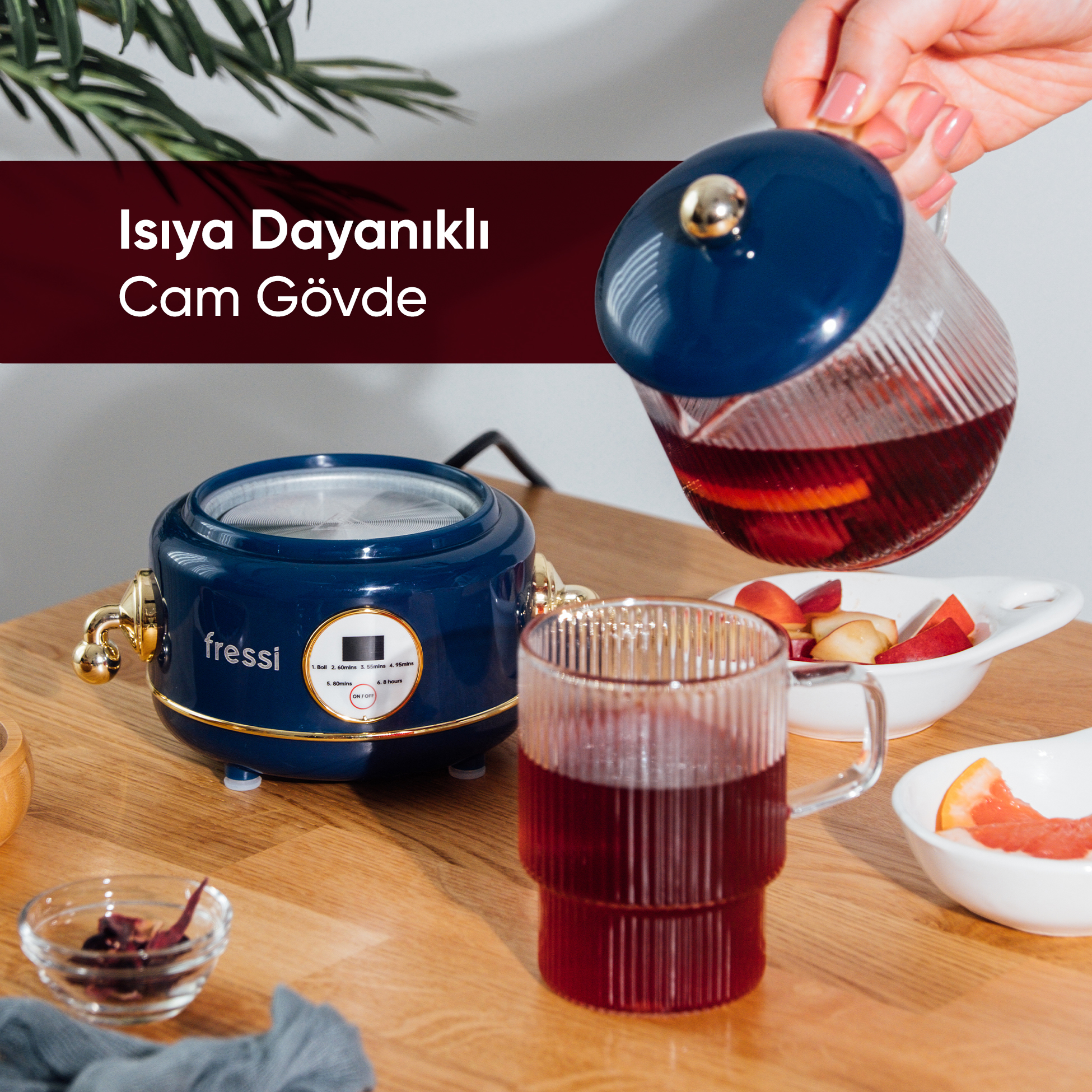 Bir el, mavi çaydanlıktan mavi bir cihazın yanındaki bardağa kırmızı içecek döküyor.