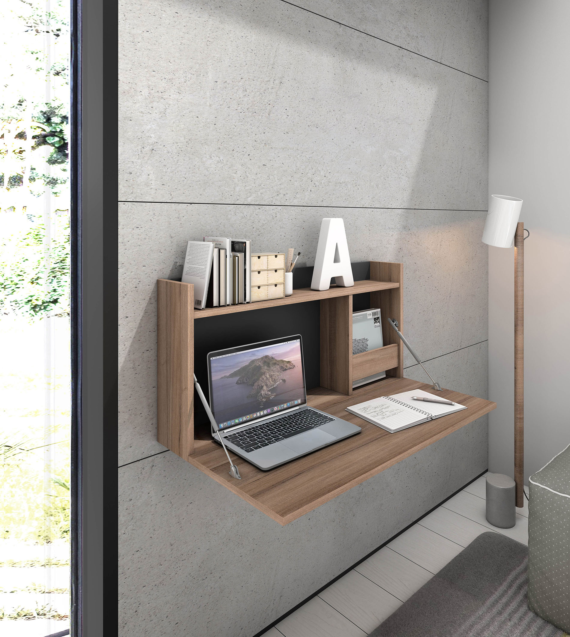 Un escritorio abatible de pared con portátil, libros y lámpara contra pared de hormigón.