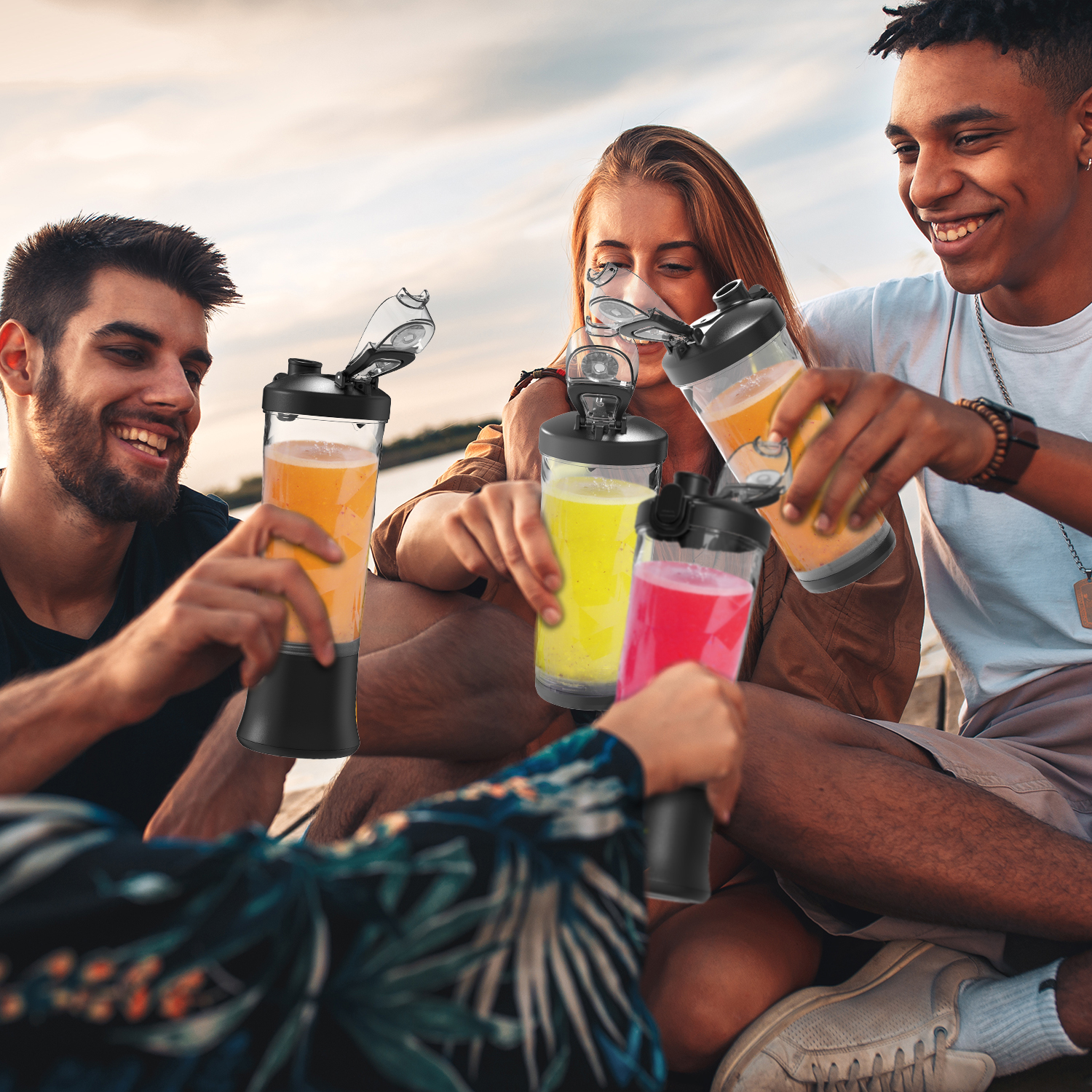 Cuatro amigos brindan con bebidas coloridas al aire libre al atardecer.
