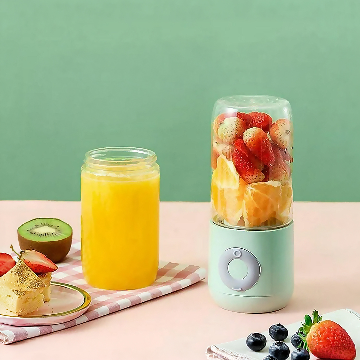 Una licuadora portátil llena de fresas y naranjas junto a un vaso de jugo de naranja.