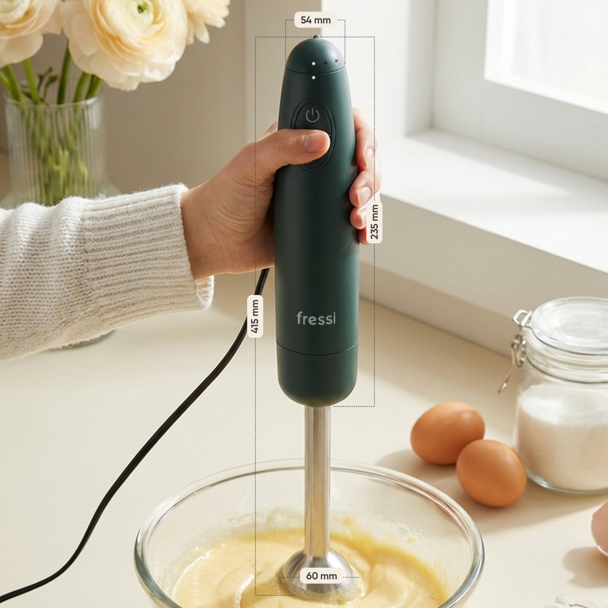 Koyu yeşil el blenderı, sarı hamurlu cam bir kasede kullanılıyor. Yakında yumurta ve şeker var.