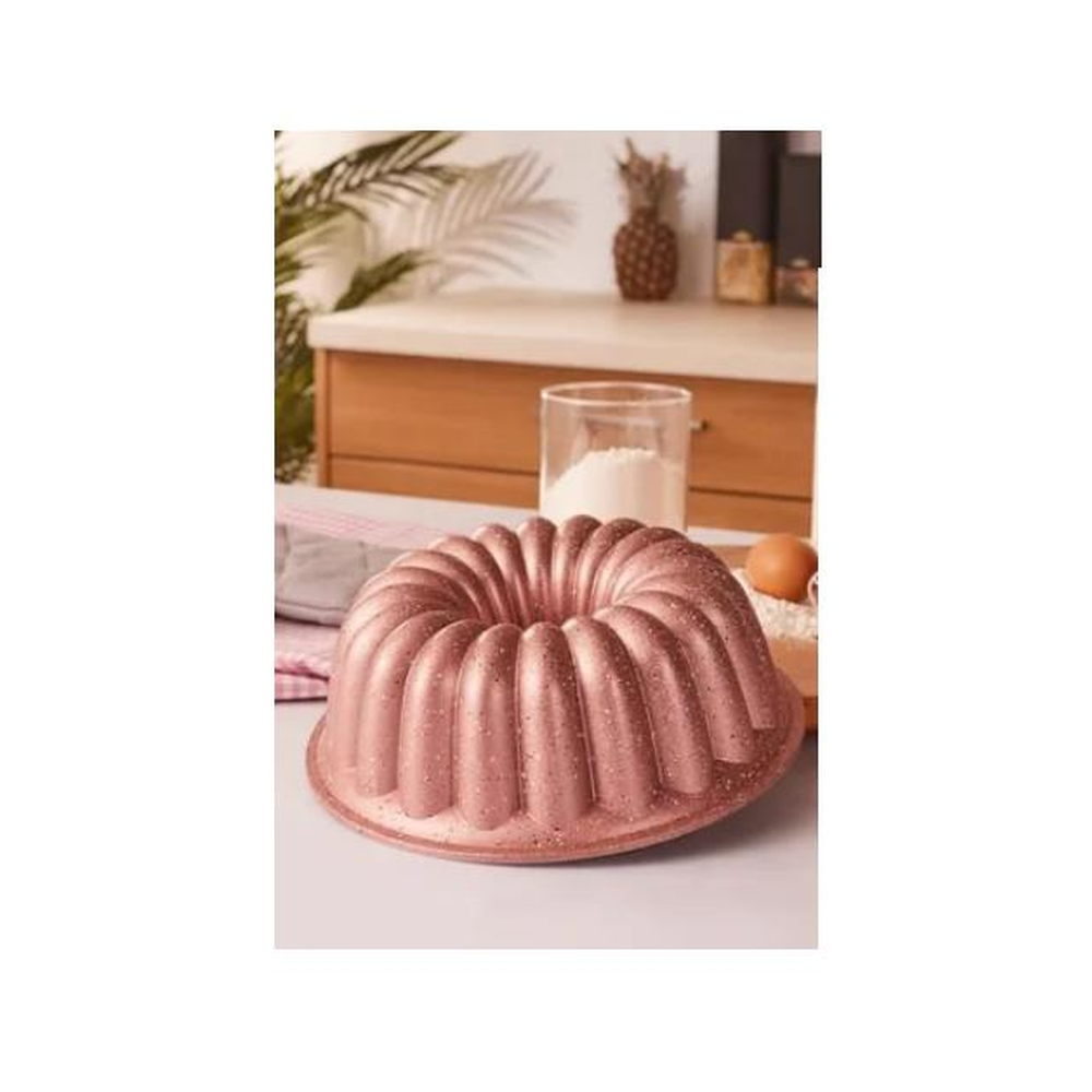 Geniş oluklu, rose gold renkte kek kalıbı, yanında un, yumurta ve mutfak bezleri.