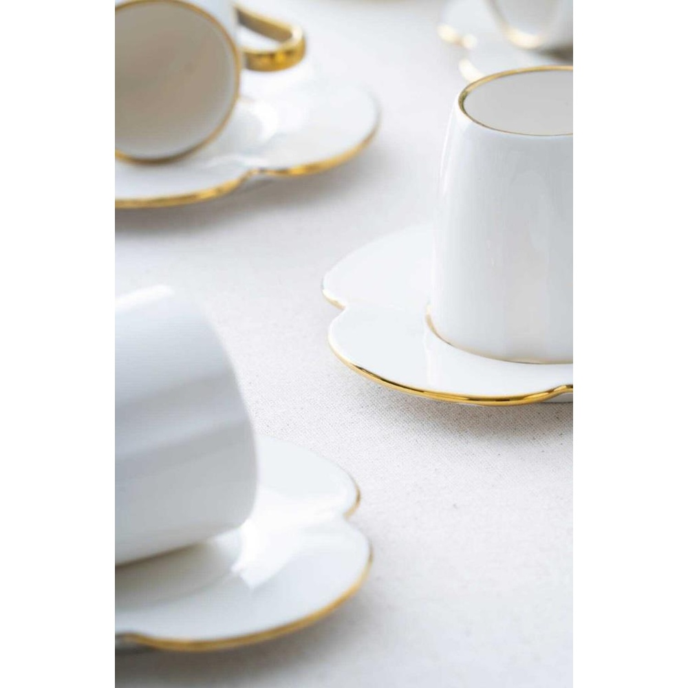 Beyaz kahve fincanları, çiçek şeklinde fincan tabakları üzerinde, beyaz masa örtüsü.